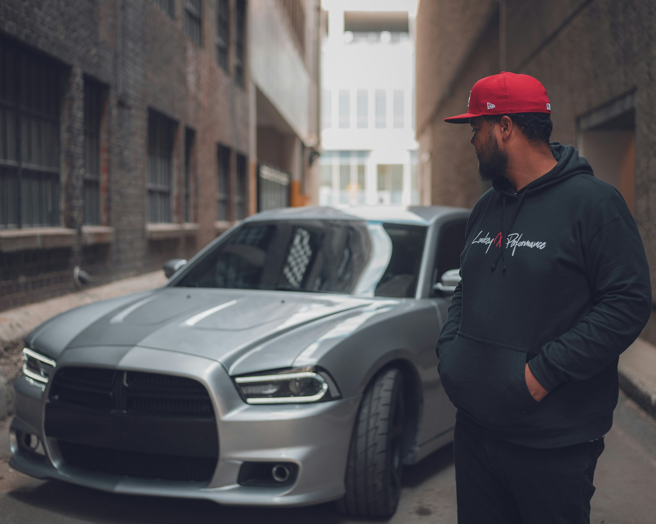 man in black jacket standing beside silver car during daytime